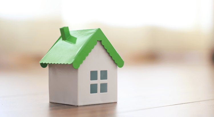 "A miniature model house with a green roof sitting on a wooden floor, representing future trends in home prices."