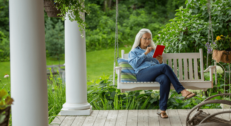 Buy Now or Wait - Senior homeowner sitting on a porch swing reading a tablet, representing lifestyle benefits of homeownership